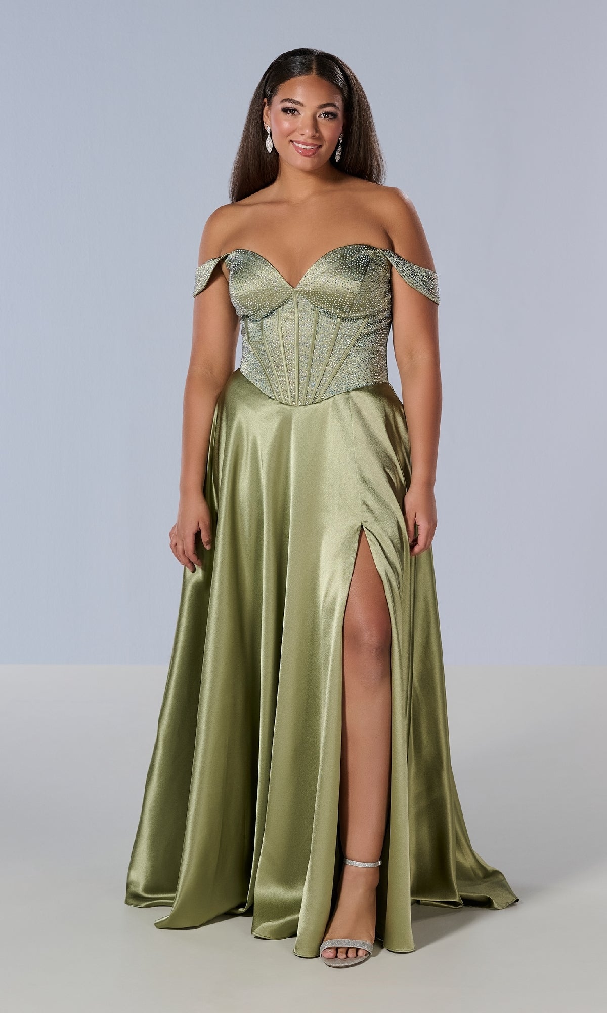 Model wearing the Tiffany 16204 long plus-size prom dress in light green satin with an off-the-shoulder neckline, structured bodice, and thigh-high slit, paired with silver heels against a plain background.